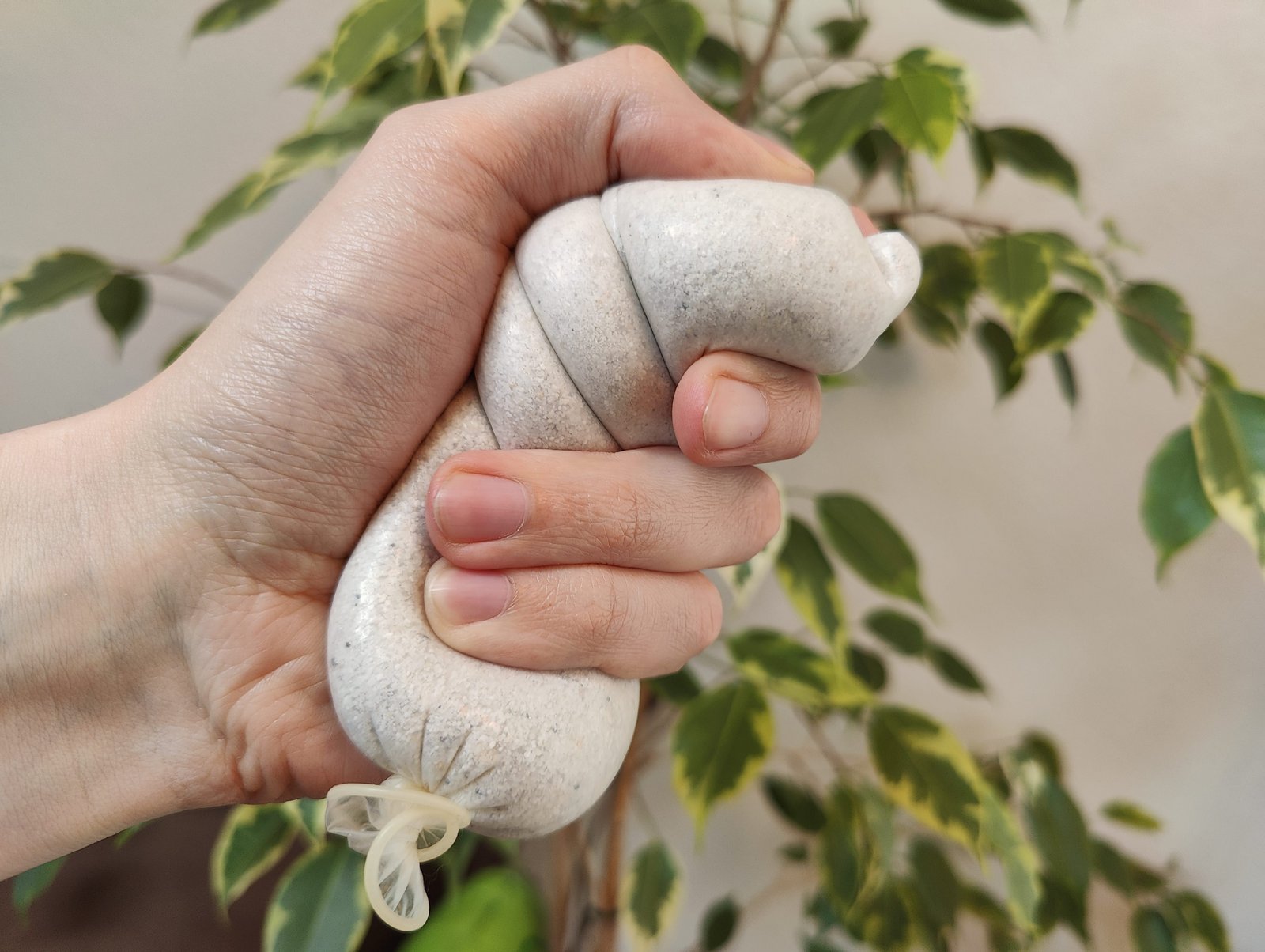 An expired condom filled with sand in the hand of someone using it as a stress ball